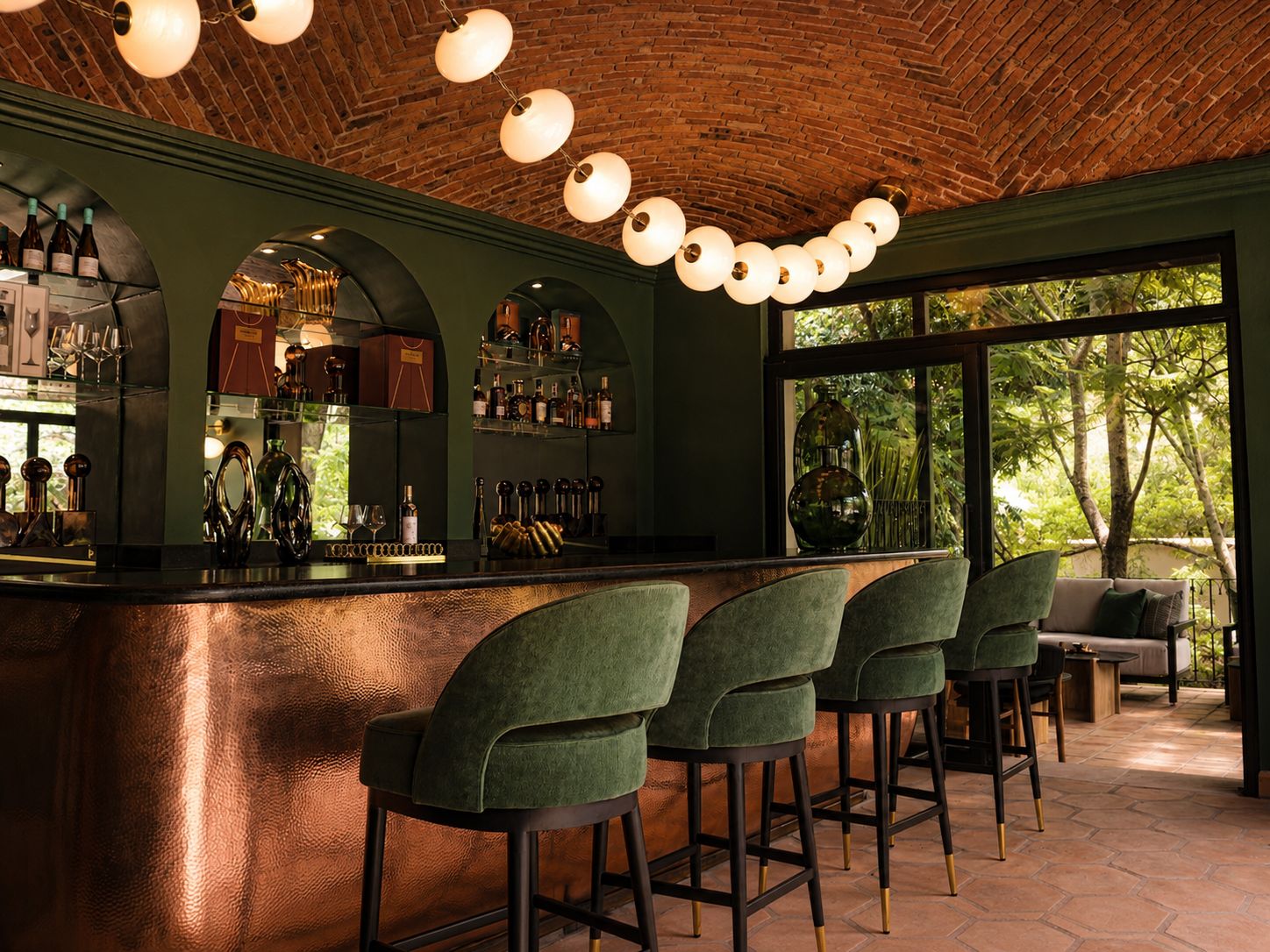 A bar area with a brick ceiling, green walls, and a large window with a view of trees. There are bar stools and a counter with bottles and glasses.