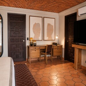 Een hotelkamer met een bakstenen plafond, een bed met een gestreept hoofdeinde, een bureau met een stoel, een televisie en kunst aan de muur.