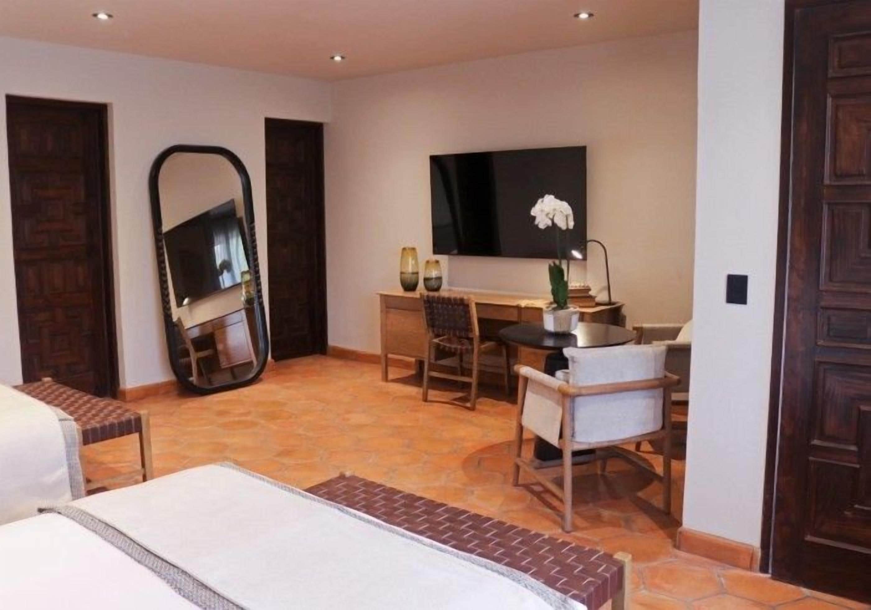 A hotel room with a bed, a desk, a chair, a television, and a large mirror.