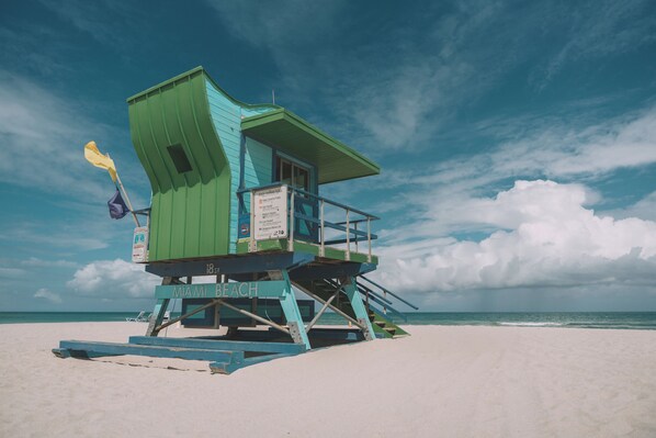 A lifeguard tower with a sign indicating beach warnings, located on a sandy beach with the ocean in the background.