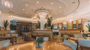 A spacious restaurant with wooden tables and booths, hanging spherical light fixtures, and a bar area with a television. - Iberostar Waves Berkeley Shore (Miami Beach)