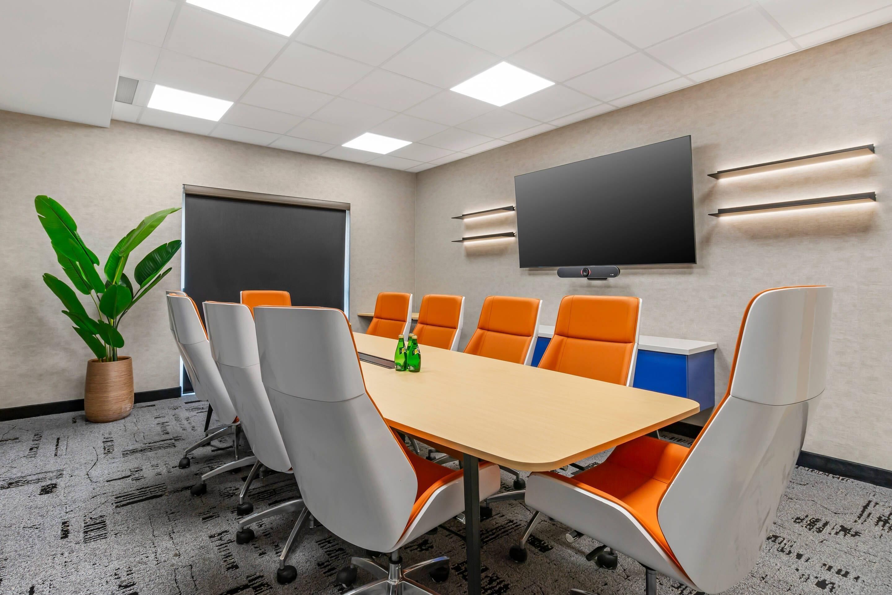A conference room with a large table, six chairs, a television, and a potted plant.