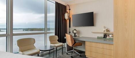 Habitación de hotel con un ventanal grande, escritorio, dos sillas, cama y televisor.