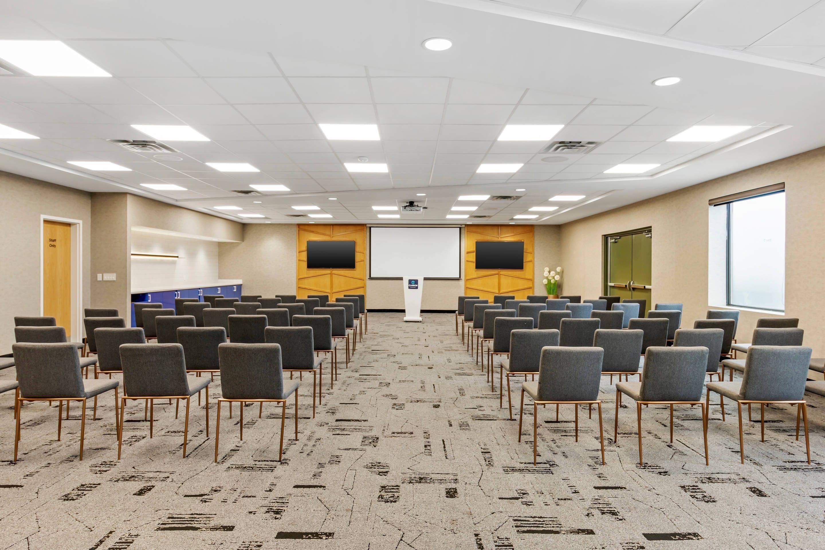 A conference room with rows of chairs, a projector screen, and a podium.