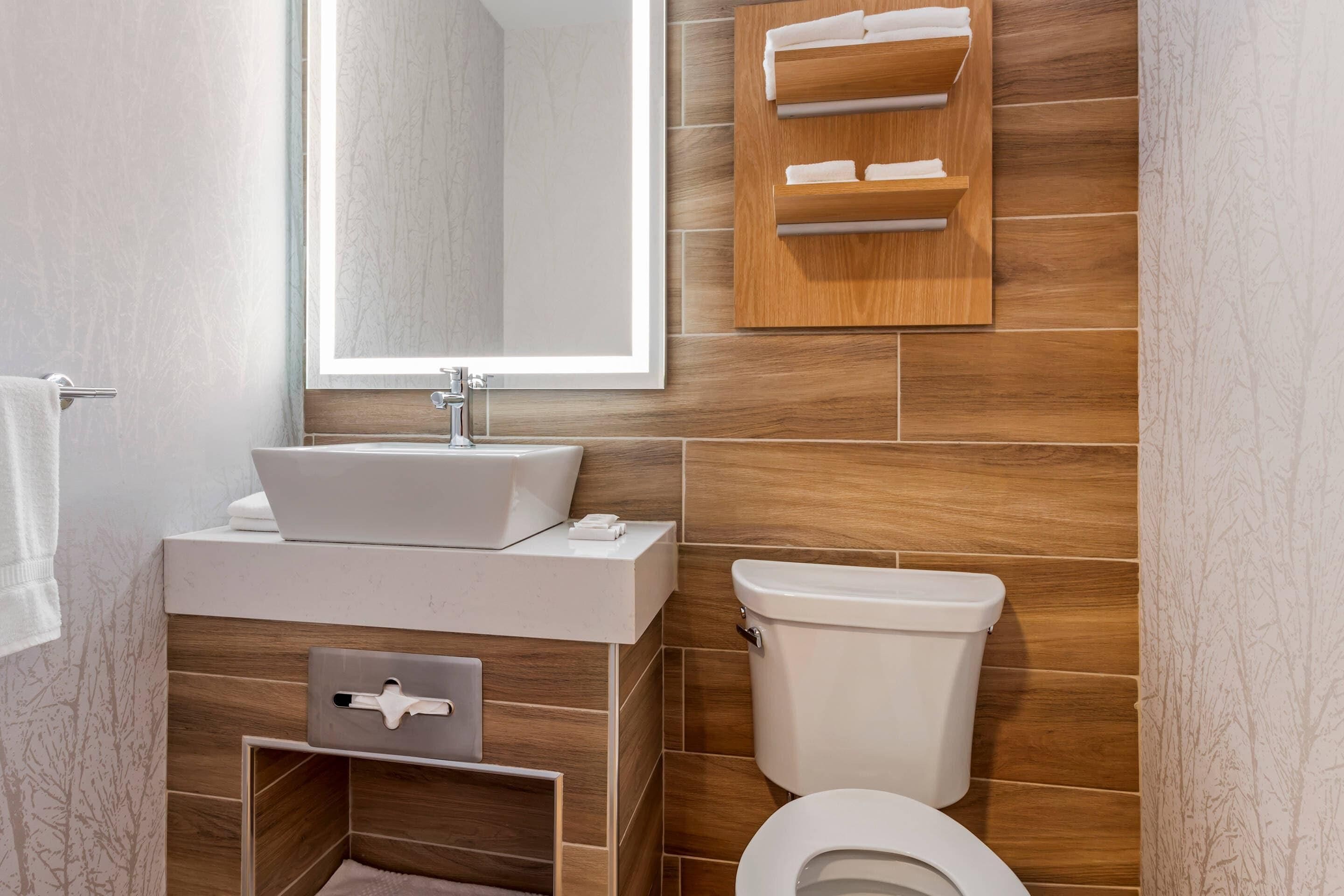 Un baño moderno con un espejo grande, un lavabo, un inodoro y un perchero para toallas.