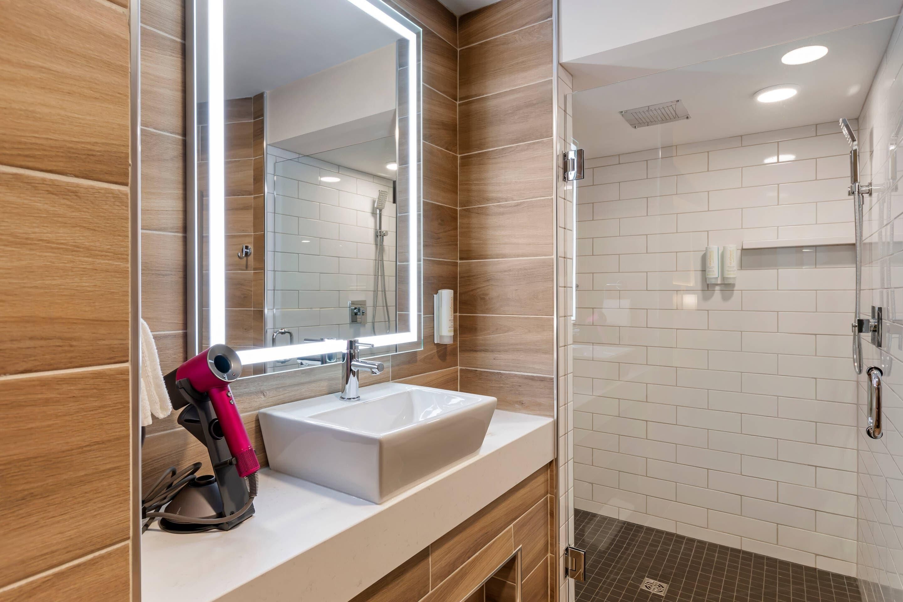 A modern bathroom with a large mirror, a sink, and a shower area.