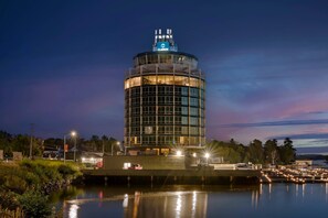 A modern hotel with a circular design, located near a waterfront with boats docked.