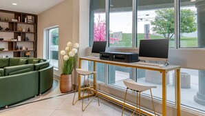 Una sala moderna con un sofá verde, una estantería de madera y un ventanal con vistas a árboles, incluyendo un árbol de flores rosadas.