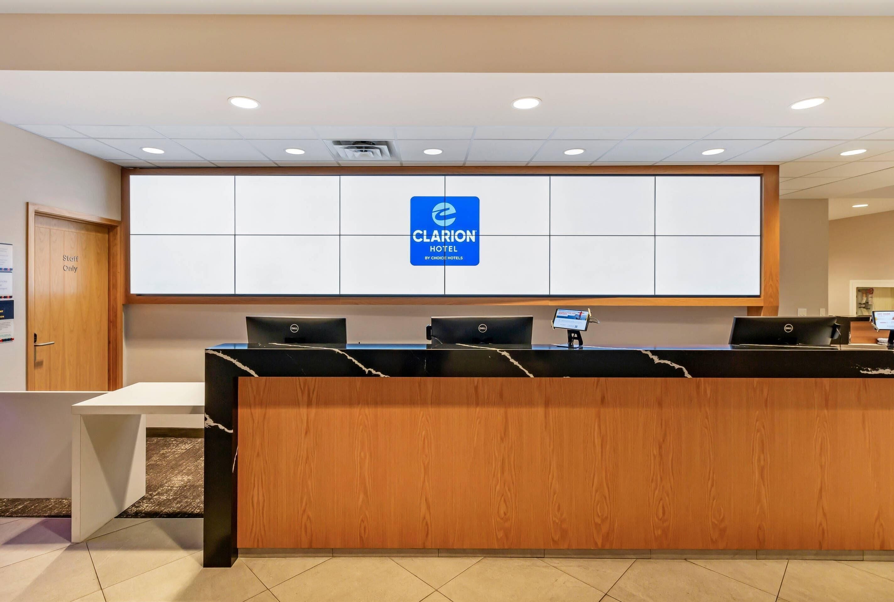 A hotel reception desk with a sign for Clarion Hotel, three computer monitors, and a wooden counter.