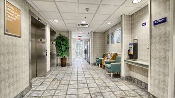 A hotel lobby with a tiled floor, elevators, a reception desk, and a 'Lobby' sign.