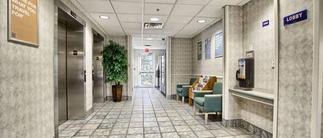A hotel lobby with a tiled floor, elevators, a reception desk, and a 'Lobby' sign.