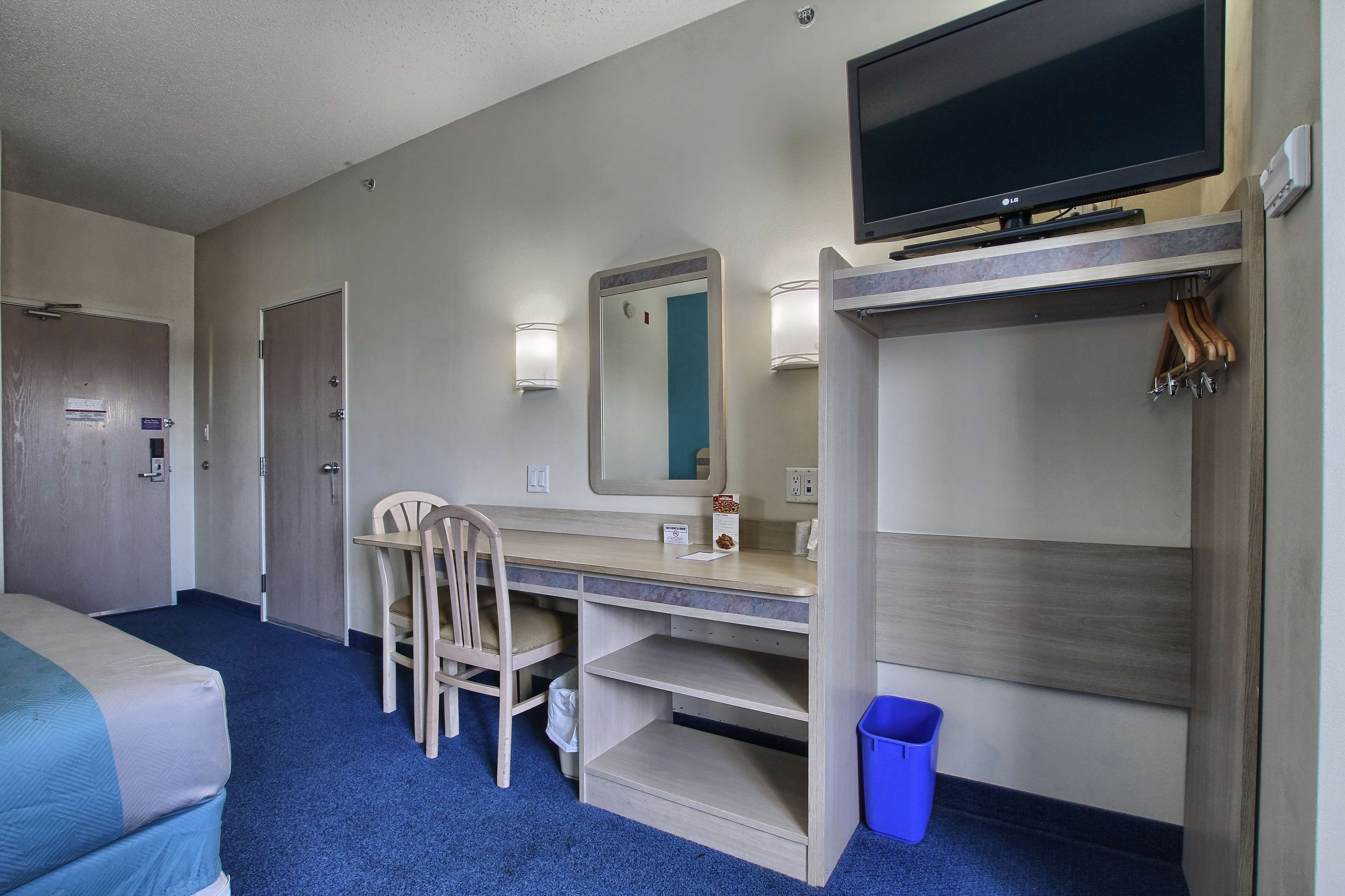 A hotel room with a bed, a desk with a chair, a TV, a mirror, and a wardrobe.