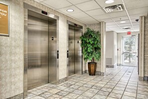 A modern elevator area with metallic elevators, a potted plant, and a tiled floor. - Motel 6 London, ON - Ontario (London)