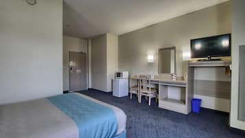 A hotel room with a bed, a desk, a chair, a television, a microwave, and a trash bin.