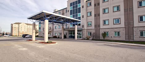 A hotel with a covered entrance, a large parking lot, and a multi-story building with a '6' logo.