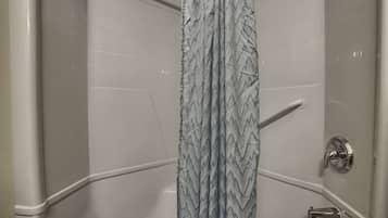 A corner of a bathroom with a shower curtain, a handrail, and a showerhead.