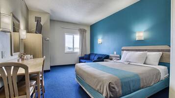 Habitación de hotel con cama, escritorio, silla, ventana con cortinas y lámpara de pared.