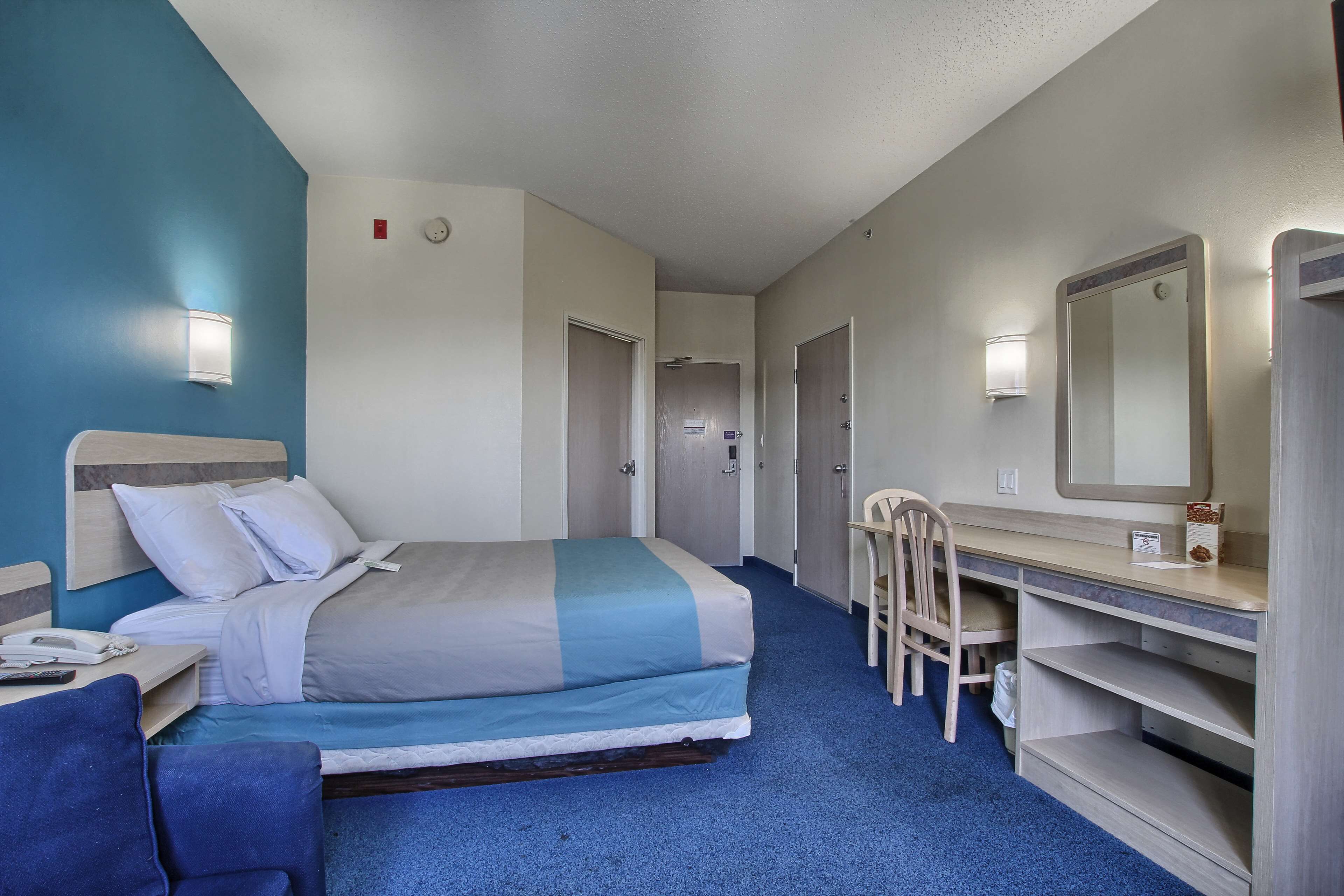 Habitación de hotel con cama, escritorio, silla y un espejo grande.