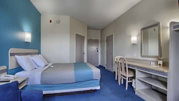 A hotel room with a bed, desk, chair, and a large mirror.
