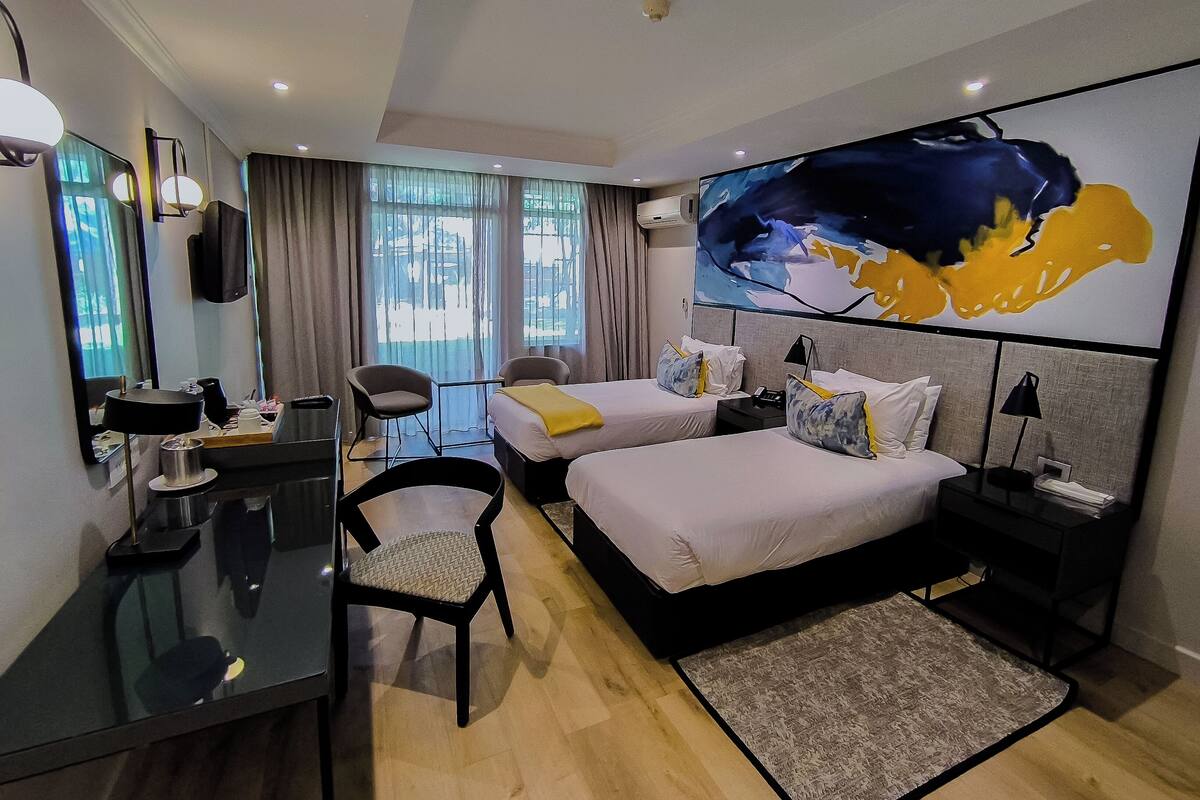 A hotel room with two beds, a desk, a chair, a TV, and a large window with curtains.