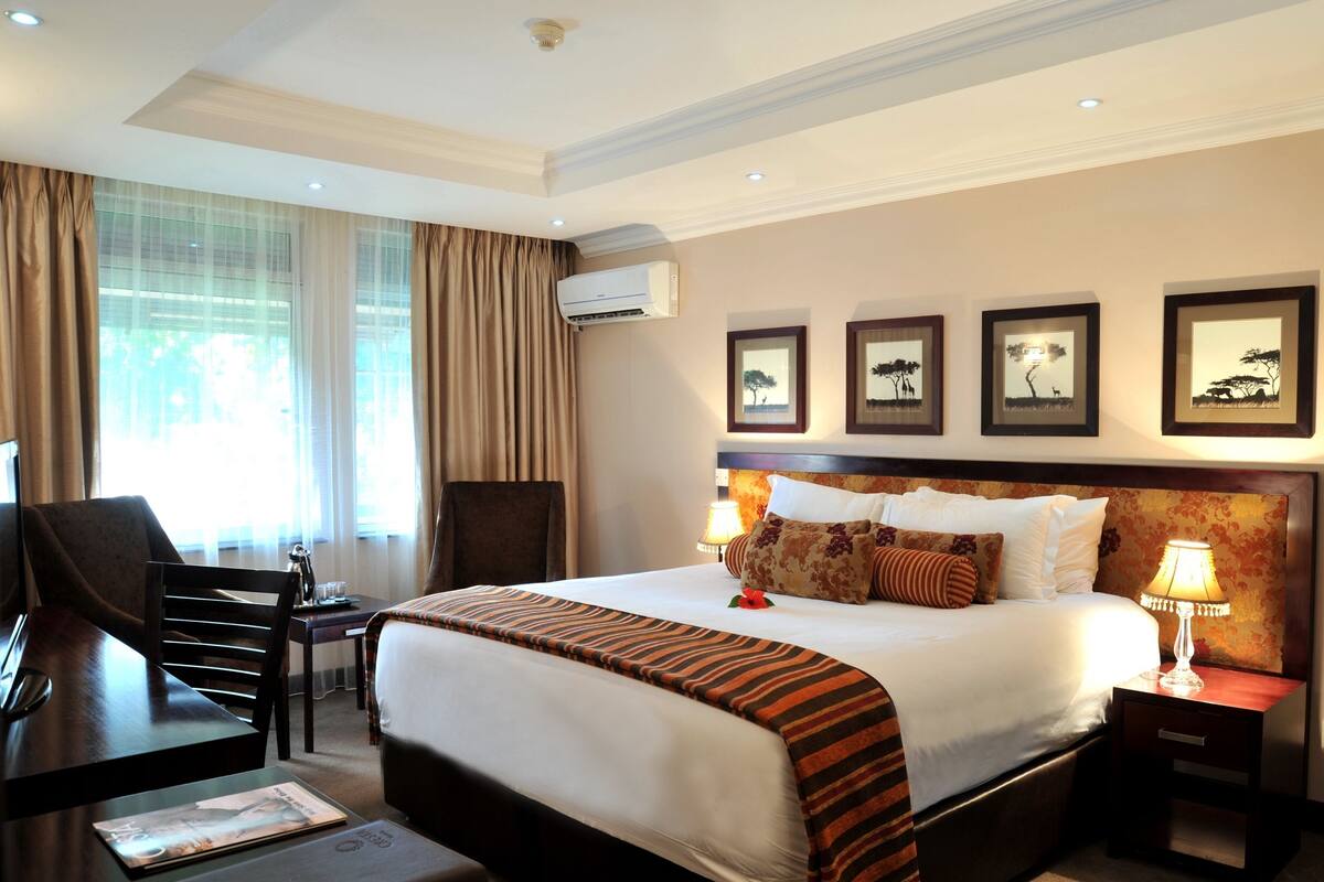 A hotel room with a bed, a desk, a chair, a lamp, and framed pictures on the wall.