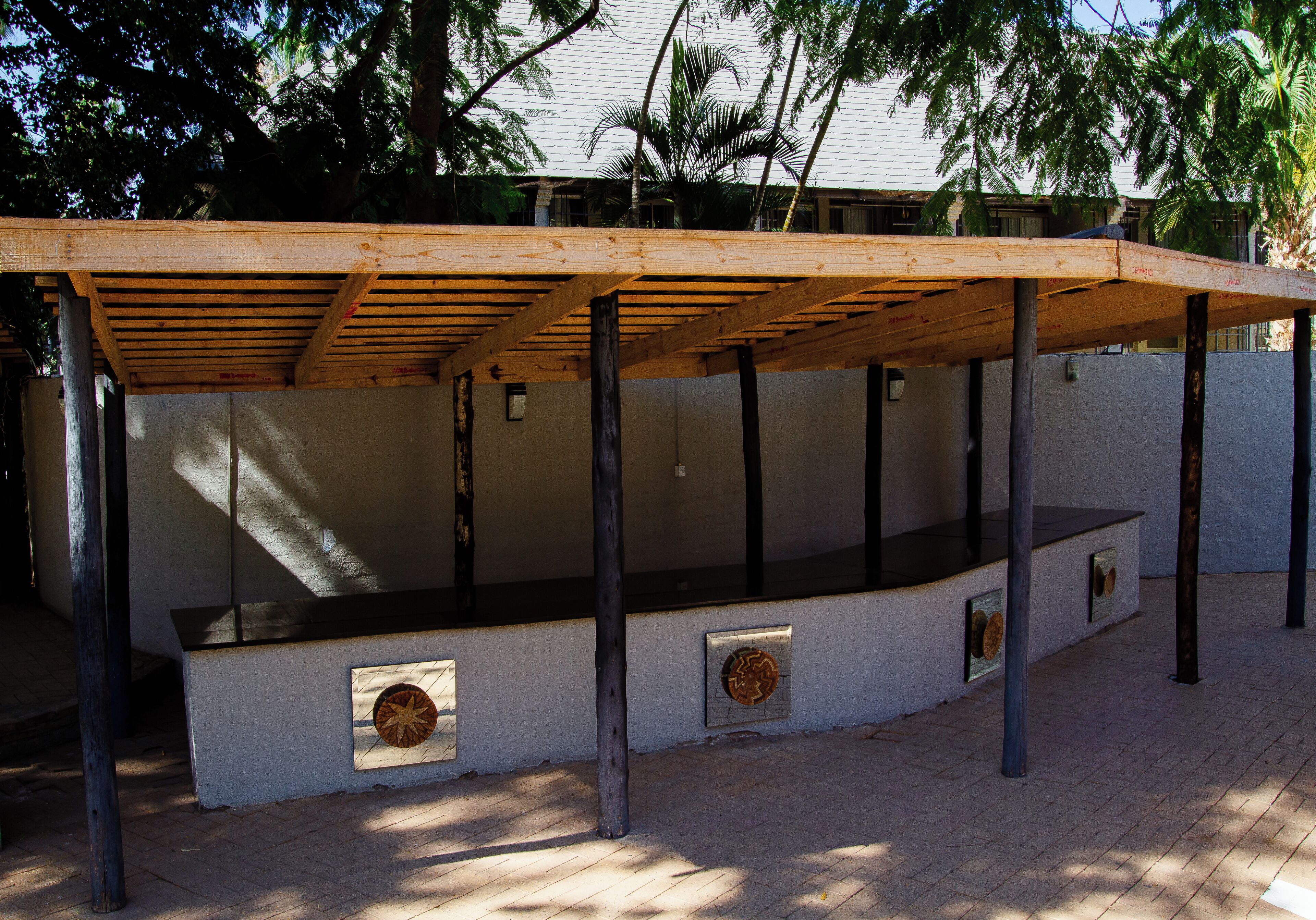 A covered outdoor area with a wooden roof supported by metal beams, featuring a bench and a wall-mounted decorative plate.