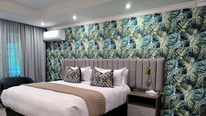 Ein modernes Schlafzimmer mit einem großen Bett, einem Nachttisch, einem Sessel und einer Wand mit einem tropischen Blattmuster.