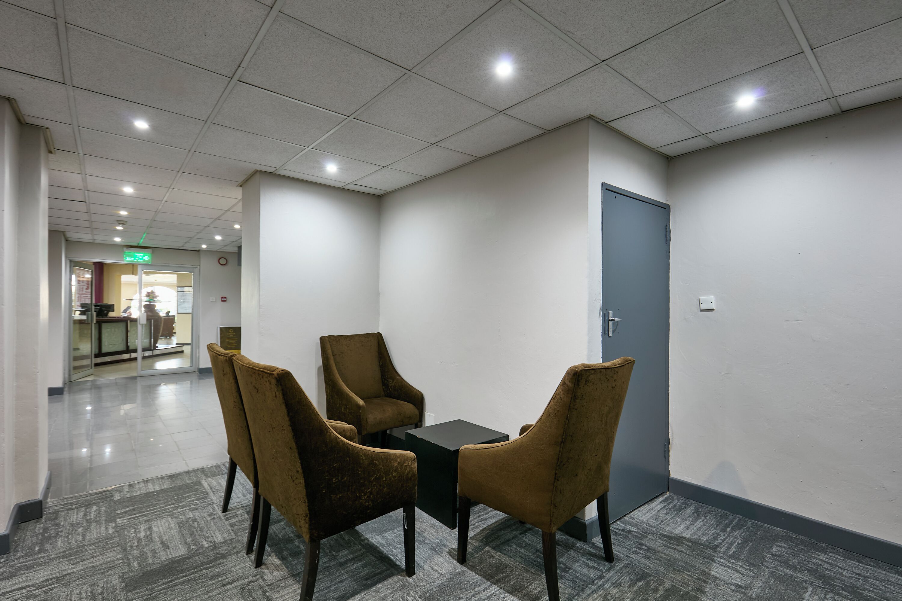 Un salón de conferencias con una mesa y cuatro sillas, una puerta y un techo con baldosas e iluminación empotrada.