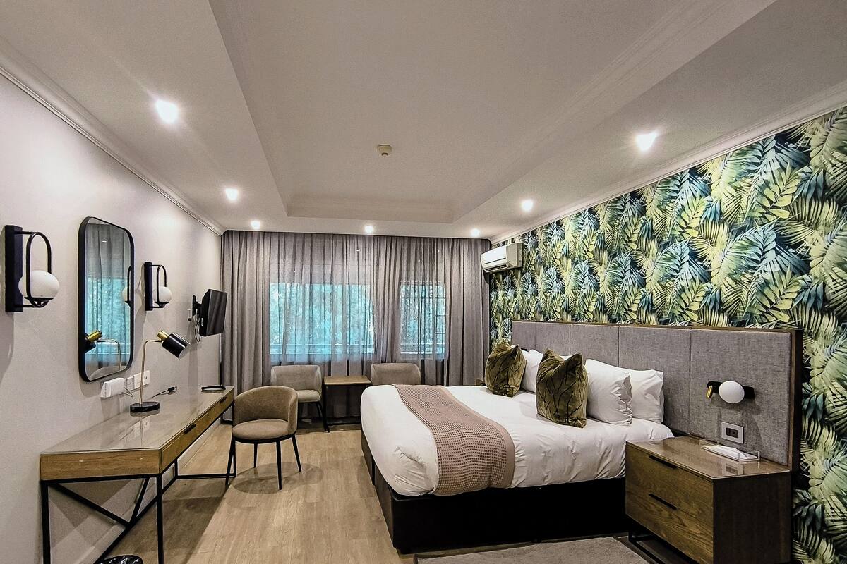 A modern hotel room with a bed, desk, chairs, and a TV.