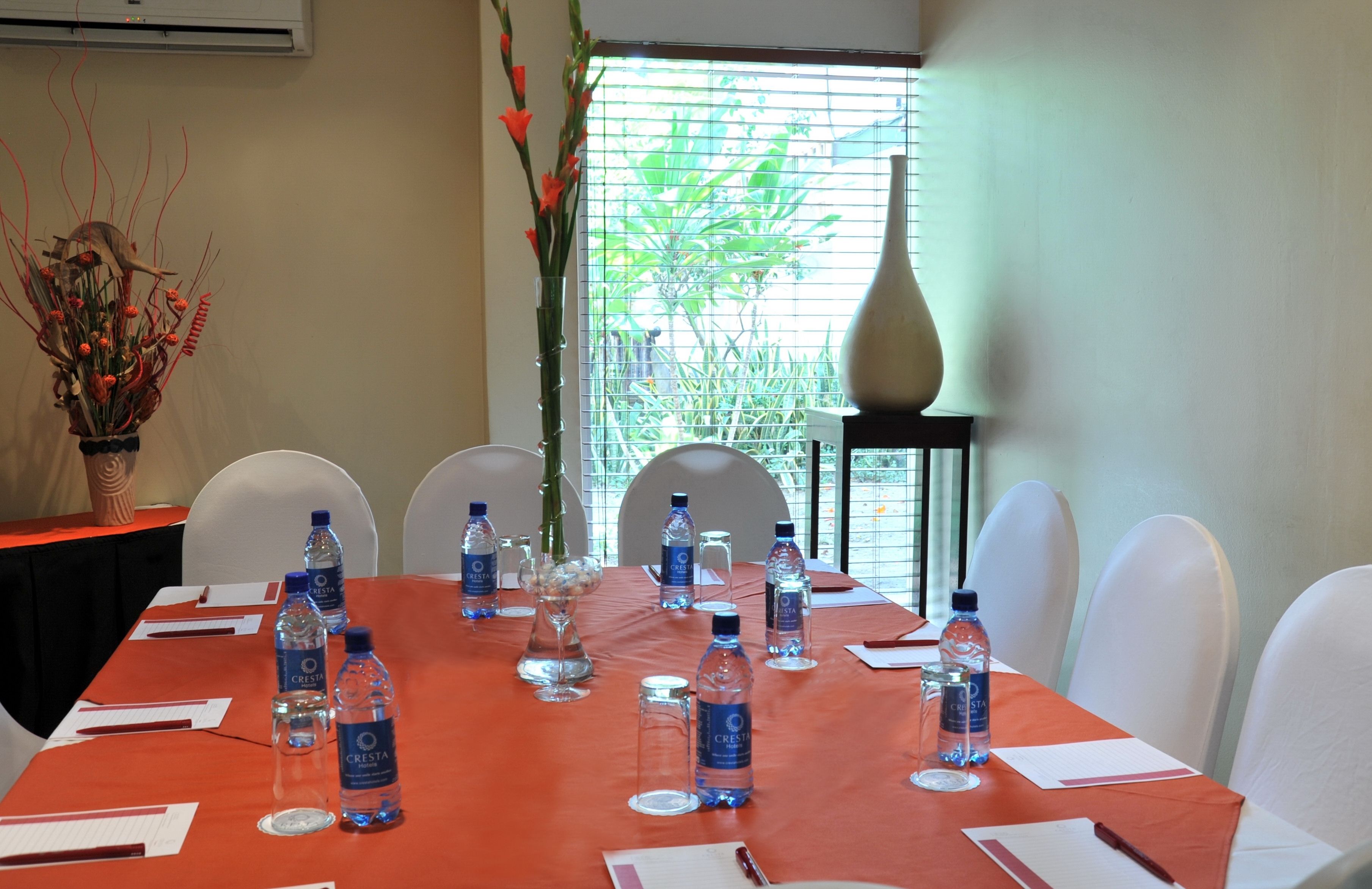 A conference room with a long table set for meetings, surrounded by white chairs.