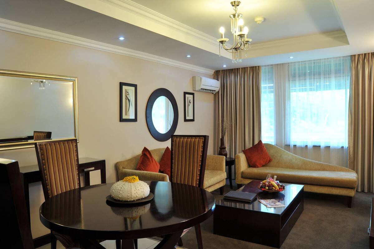 A hotel room with a dining table, chairs, a sofa, a coffee table, and a large mirror.