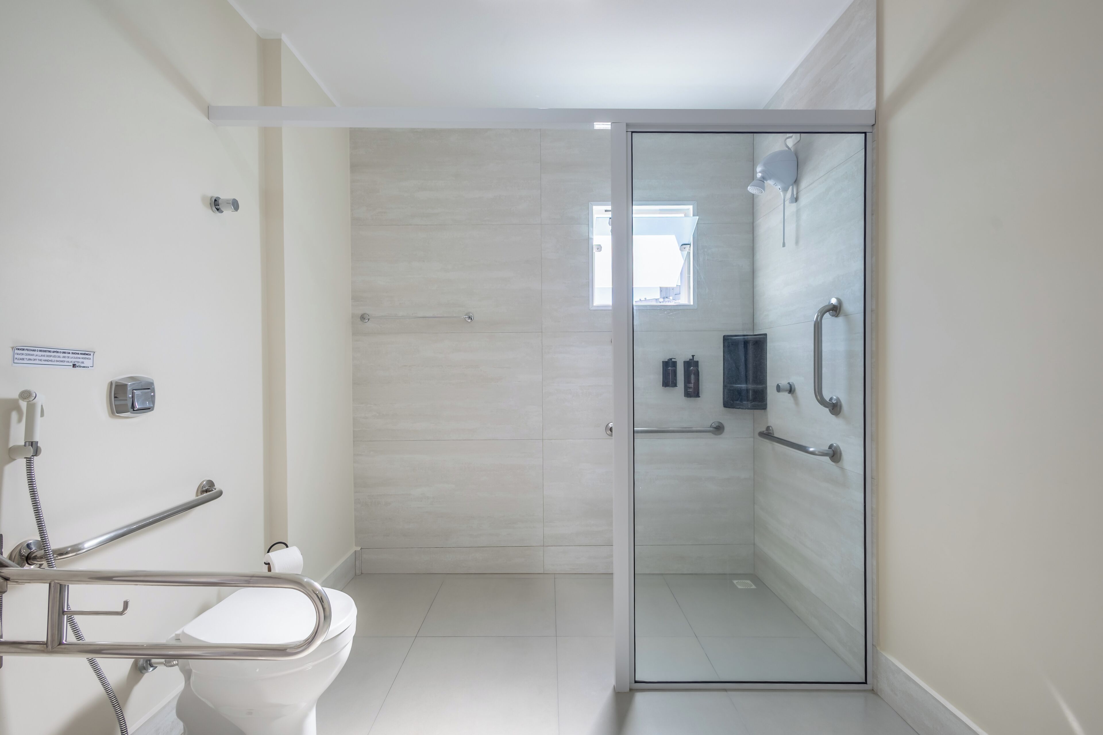 Een moderne badkamer met een douchecabine van glas, een wit toilet en een handgreep.
