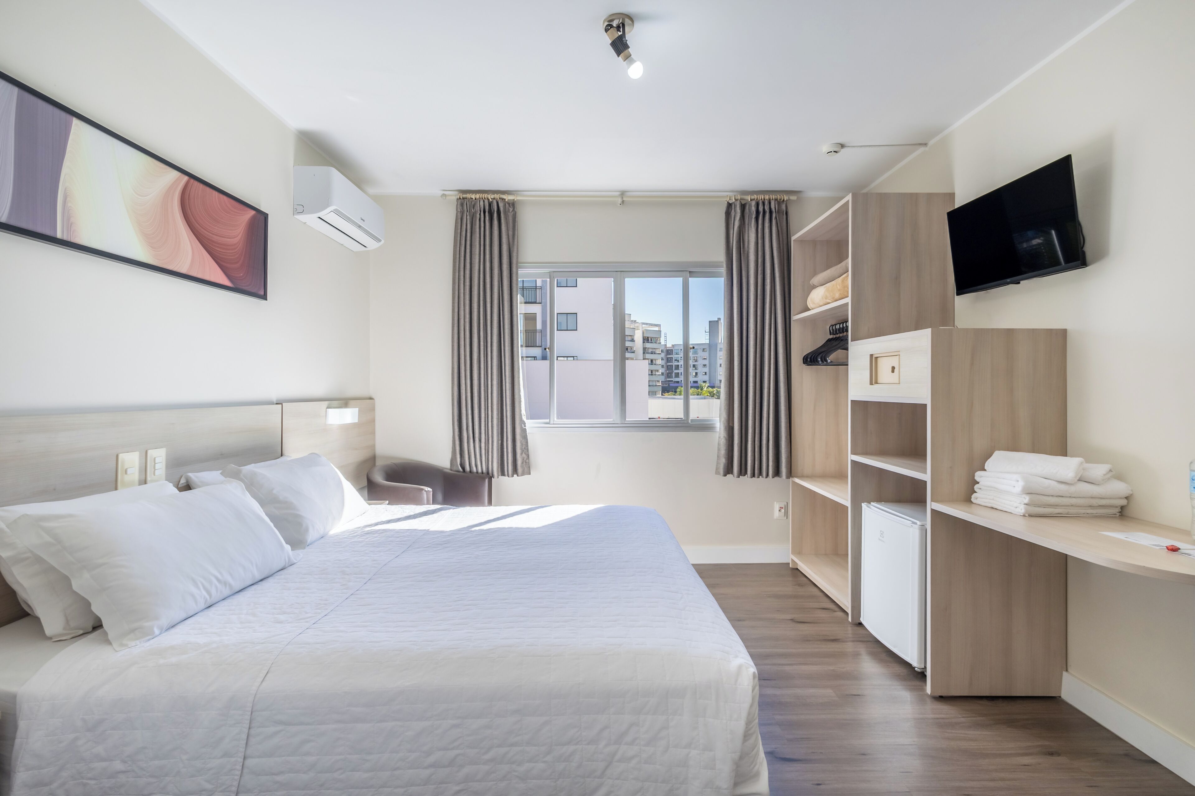 Ein Hotelzimmer mit Bett, Fernseher, Fenster mit Vorhängen, Schreibtisch und Kleiderschrank.