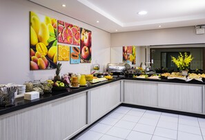 A buffet area with a variety of fruits and beverages, a coffee machine, and a large mirror. - Hotel Rosenbrock (Balneário Camboriú)