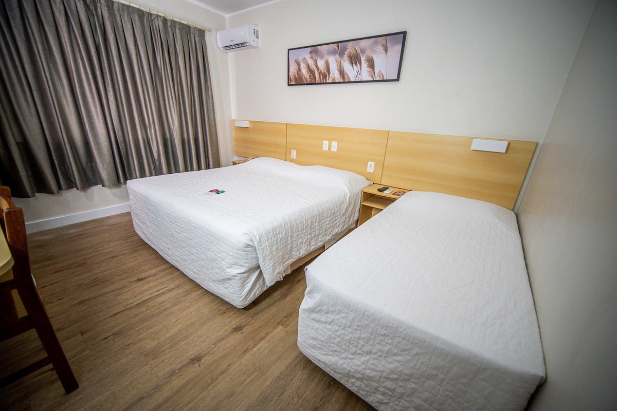 A hotel room with two beds, wooden headboard, a painting on the wall, and a wooden chair.