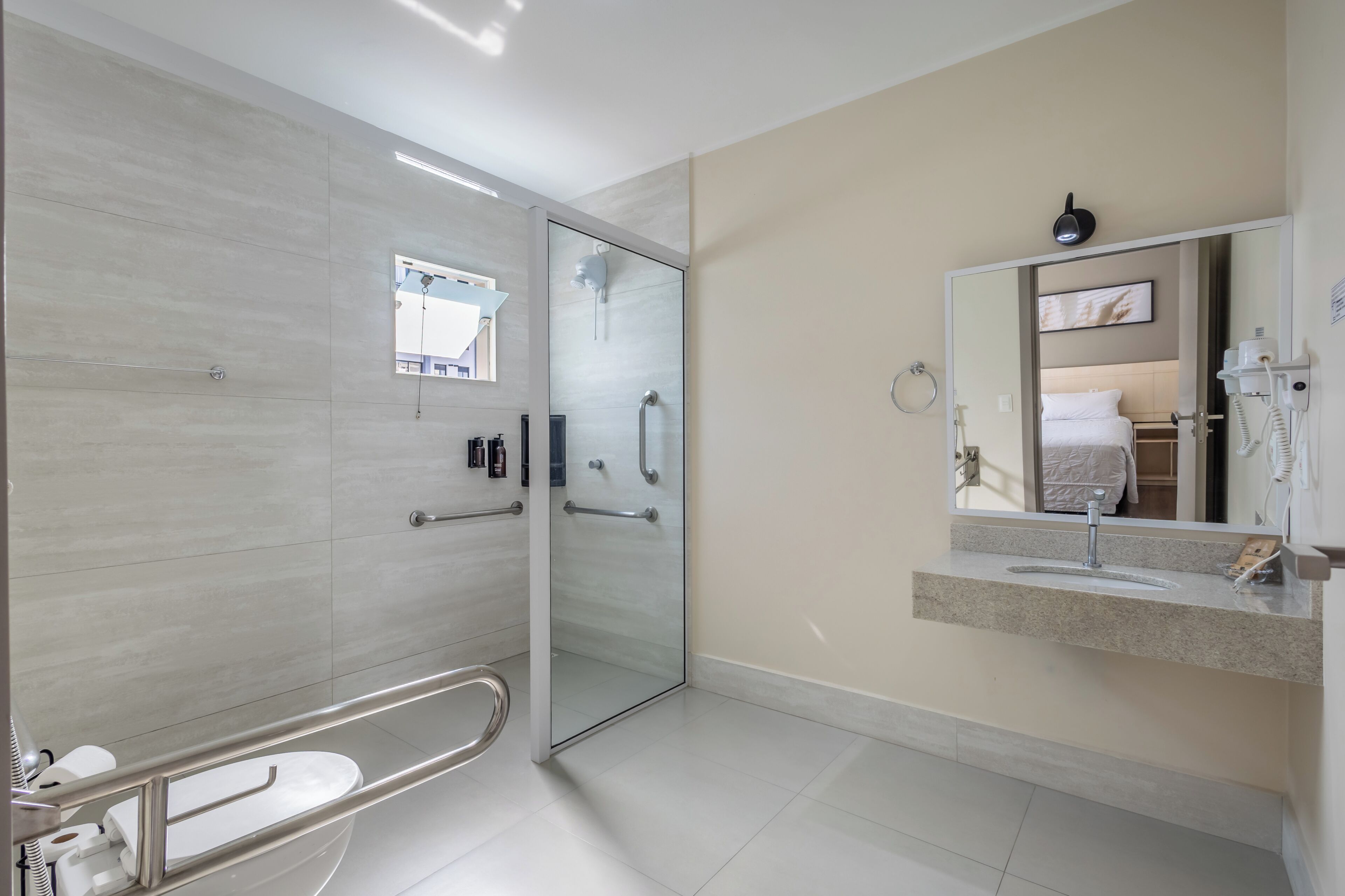 Un baño moderno con cabina de ducha de vidrio, inodoro con barra de apoyo, lavabo con espejo y teléfono.