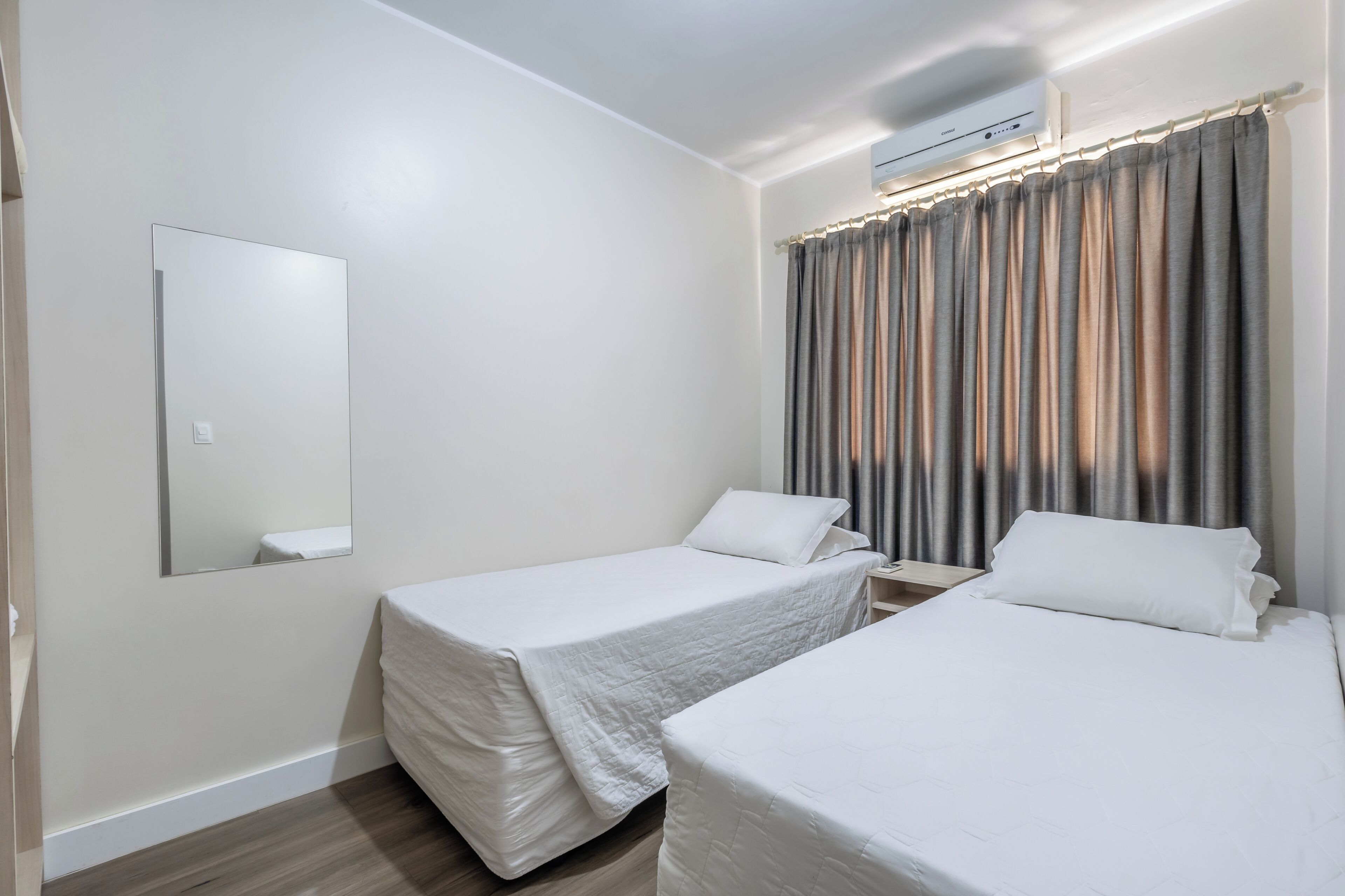Une chambre d’hôtel avec deux lits simples, un grand miroir et une fenêtre avec des rideaux.