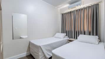 Une chambre d’hôtel avec deux lits simples, un grand miroir et une fenêtre avec des rideaux.