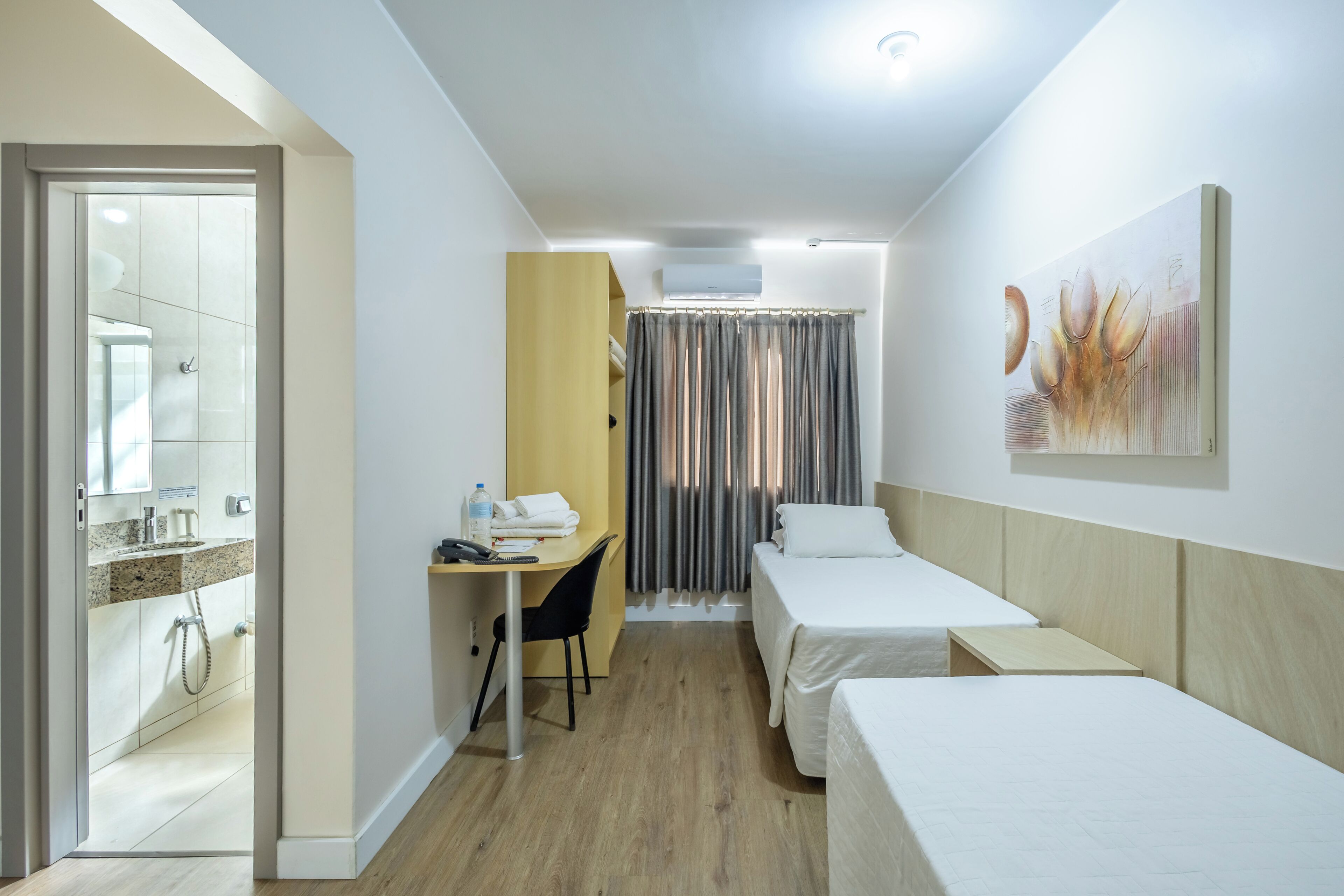 A hotel room with a shower, a desk with a chair, two beds, and a painting on the wall.
