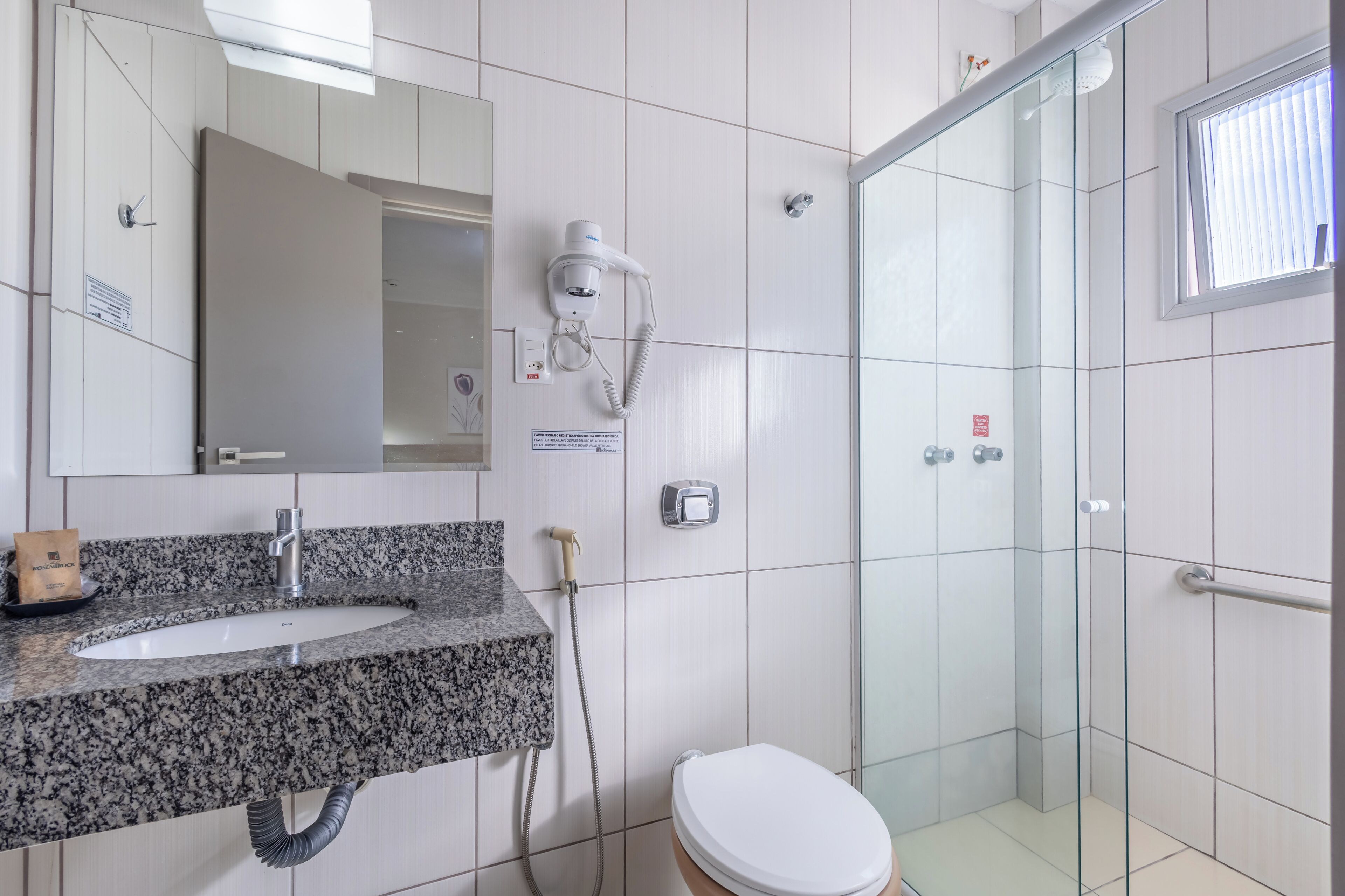 Ein Badezimmer mit Marmorwaschtisch, Duschbrause, Toilette und einer Duschkabine aus Glas.
