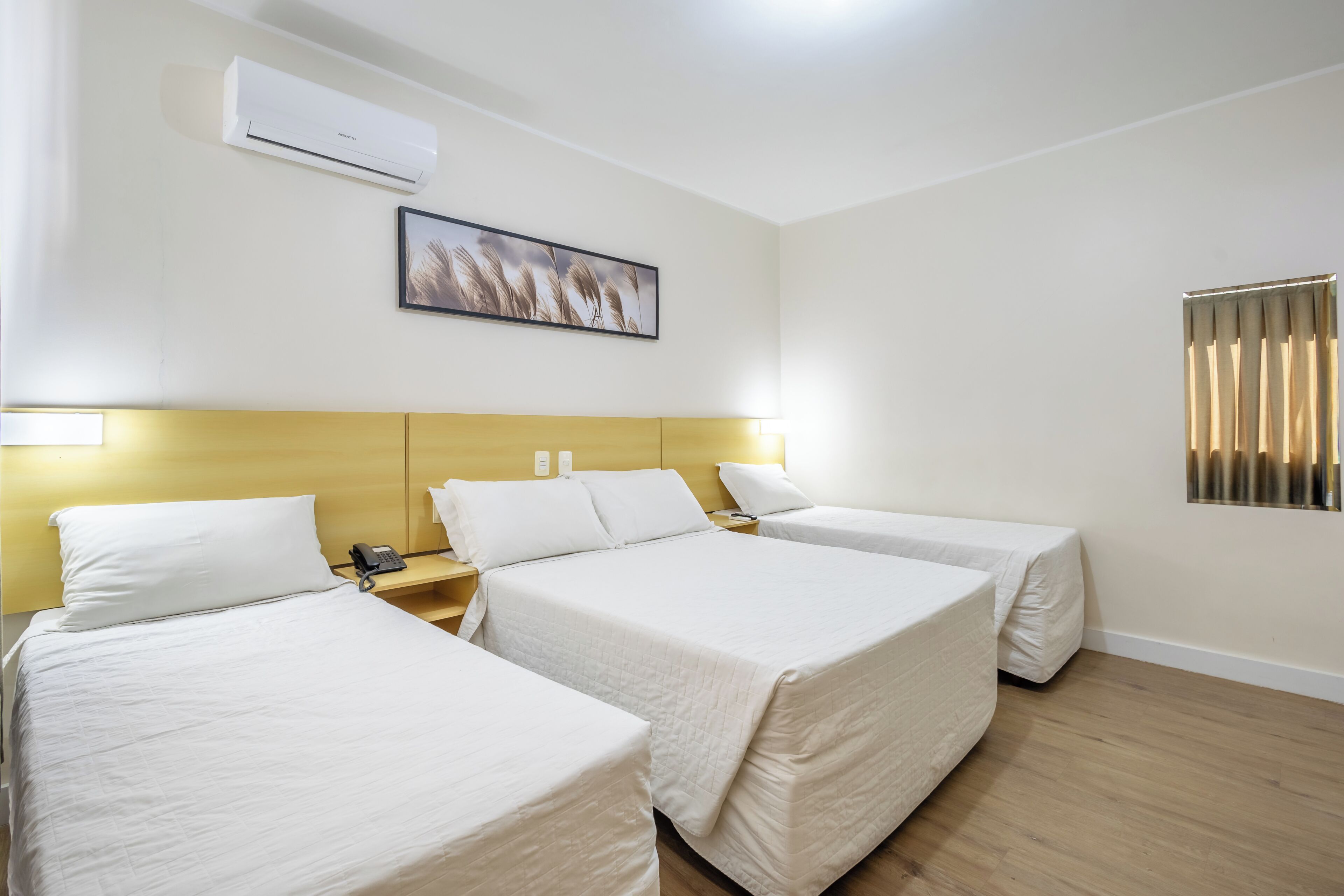A hotel room with two beds, a bedside table with a phone, an air conditioner, and a framed picture on the wall.