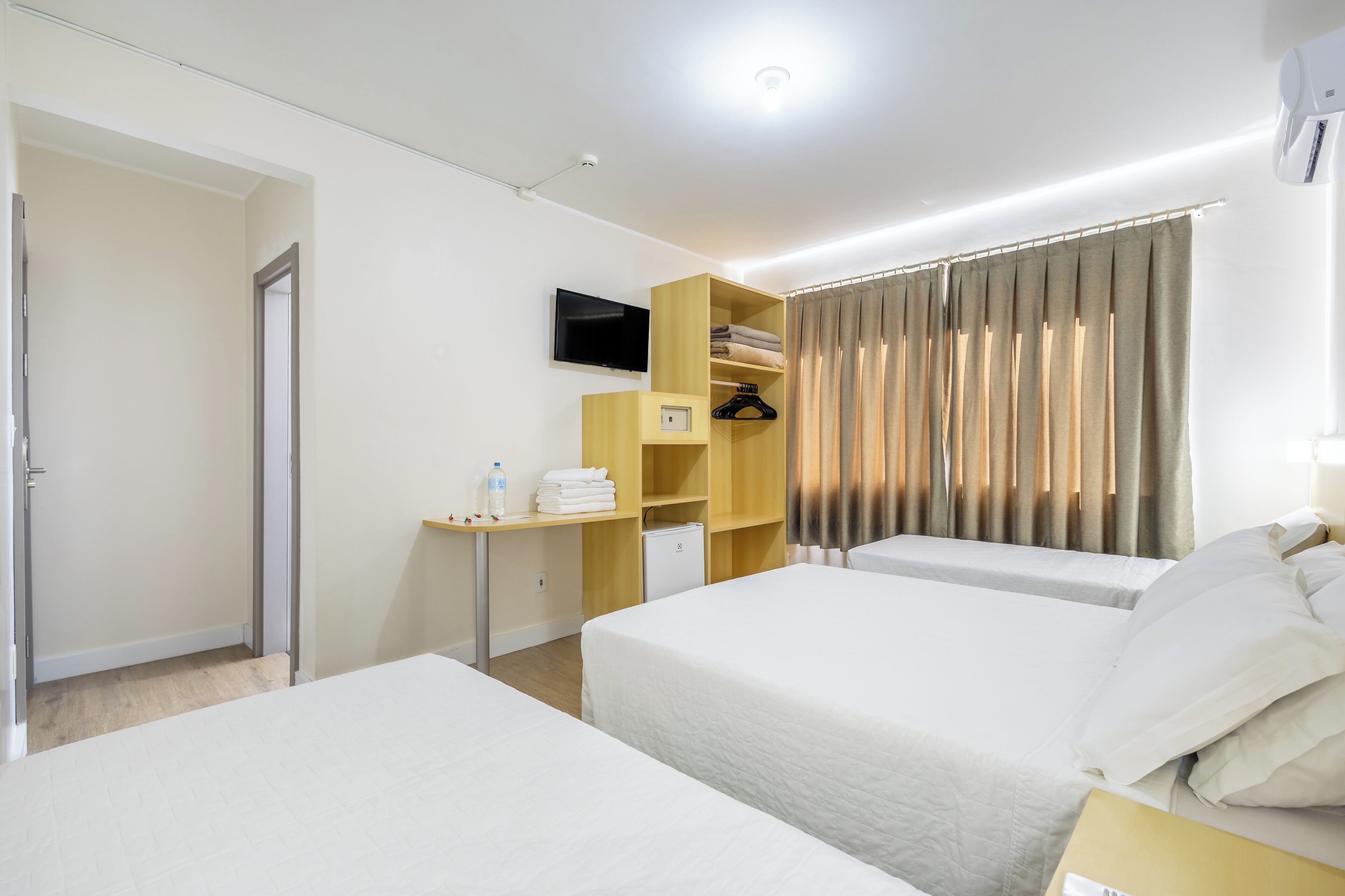 Habitación de hotel con dos camas, un televisor, un escritorio con una silla y un armario.