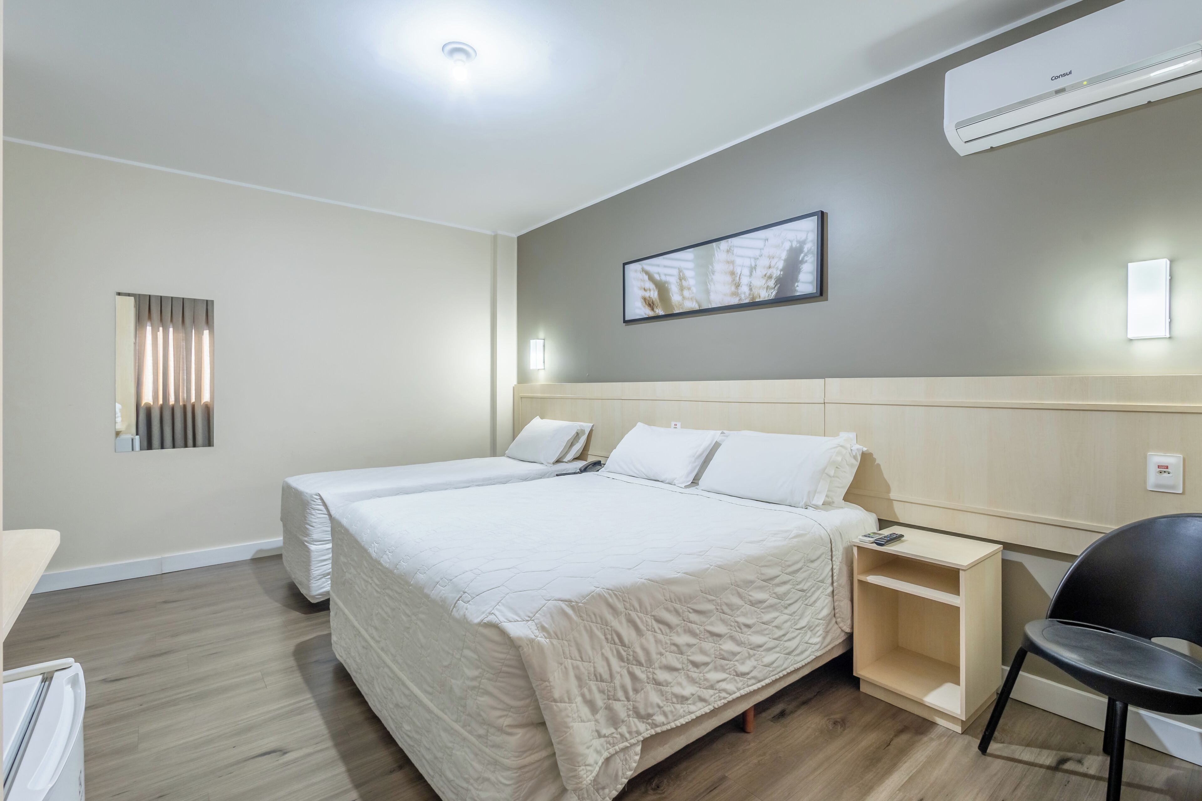 Ein Hotelzimmer mit zwei Betten, einem Nachttisch, einem Sessel, einer Wandklimaanlage und einem gerahmten Bild an der Wand.