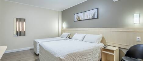 A hotel room with two beds, a bedside table, a chair, a wall-mounted air conditioner, and a framed picture on the wall.