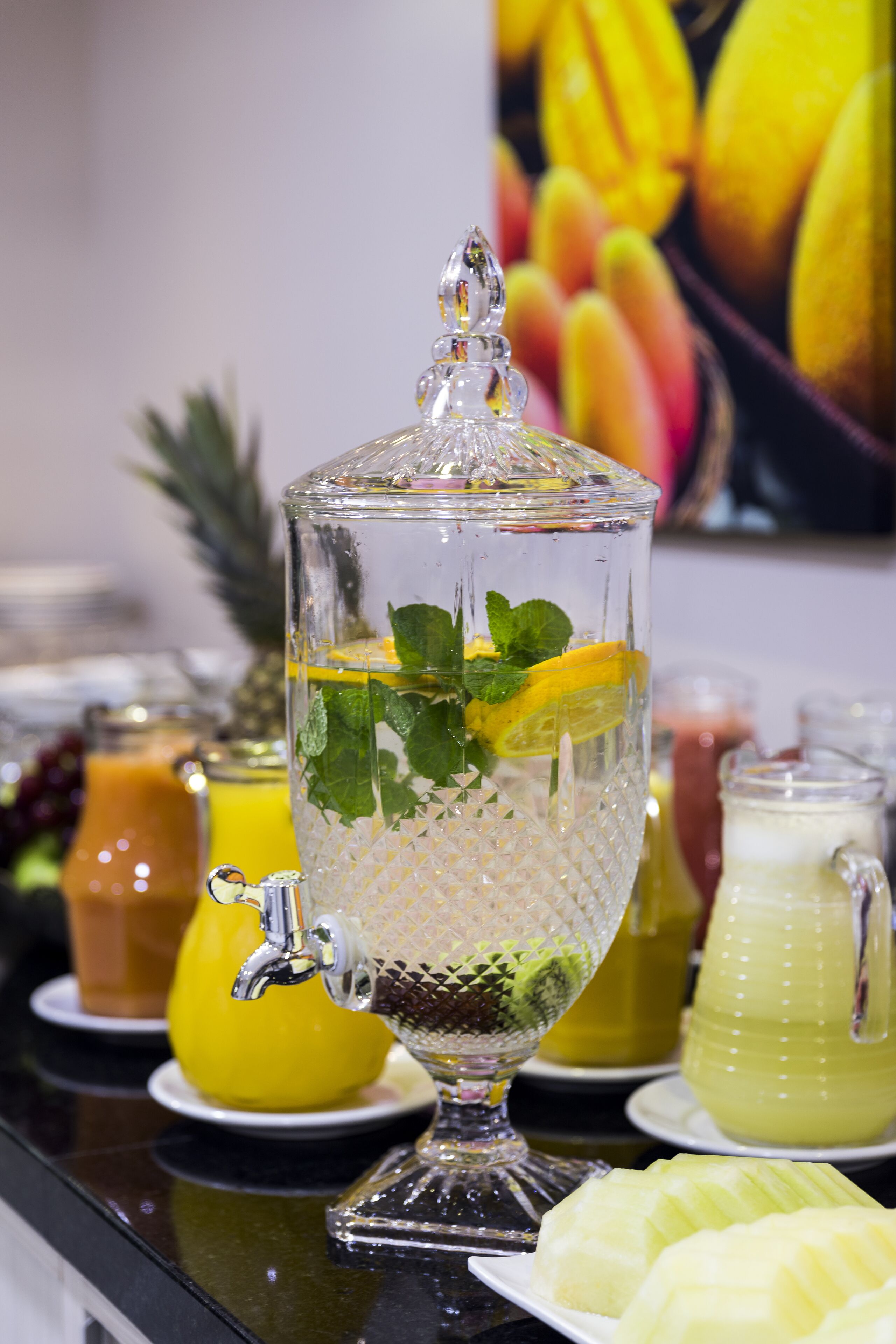 Eine transparente Punchschale mit Minzblättern und Zitronenscheiben, umgeben von verschiedenen Fruchtsäften und einer Ananas.