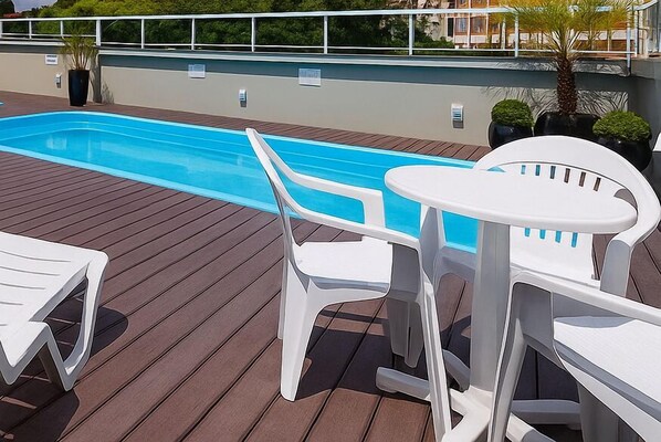 A poolside area with a wooden deck, white plastic chairs, and a small round table.