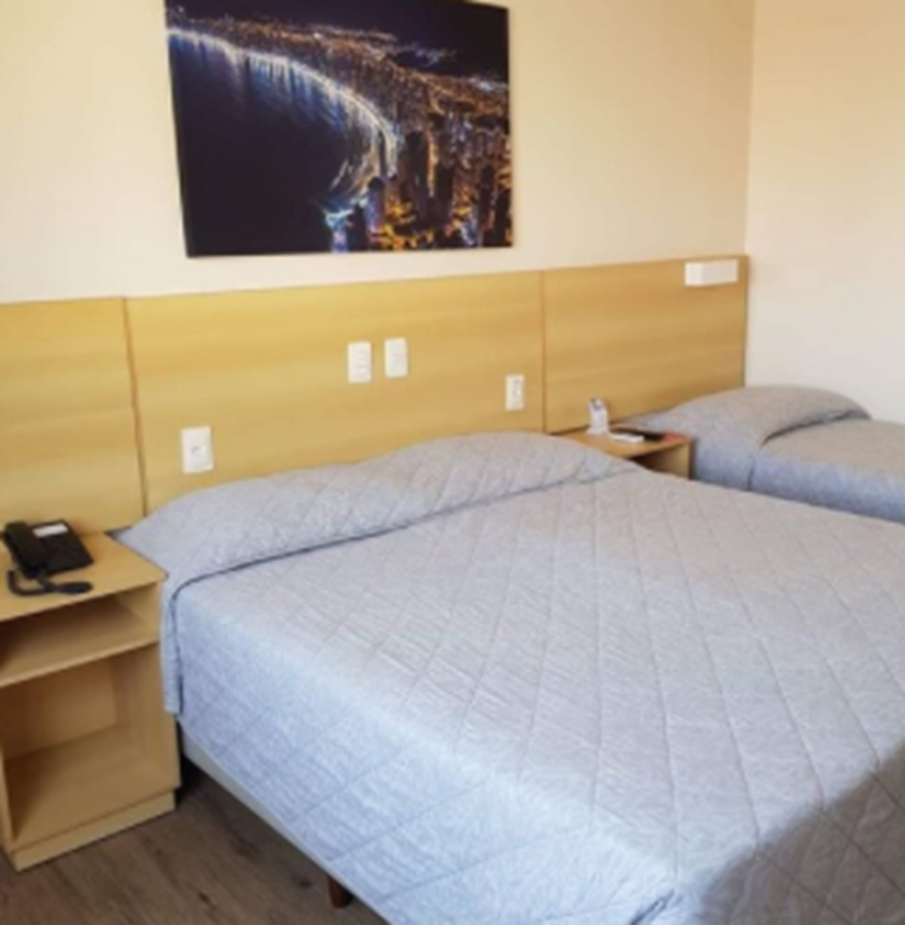 Une chambre d’hôtel avec un lit simple, une table de chevet, un téléphone et un tableau accroché au mur.