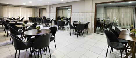 Un comedor amplio con varias mesas y sillas, que cuenta con piso de baldosas y ventanas grandes con cortinas.