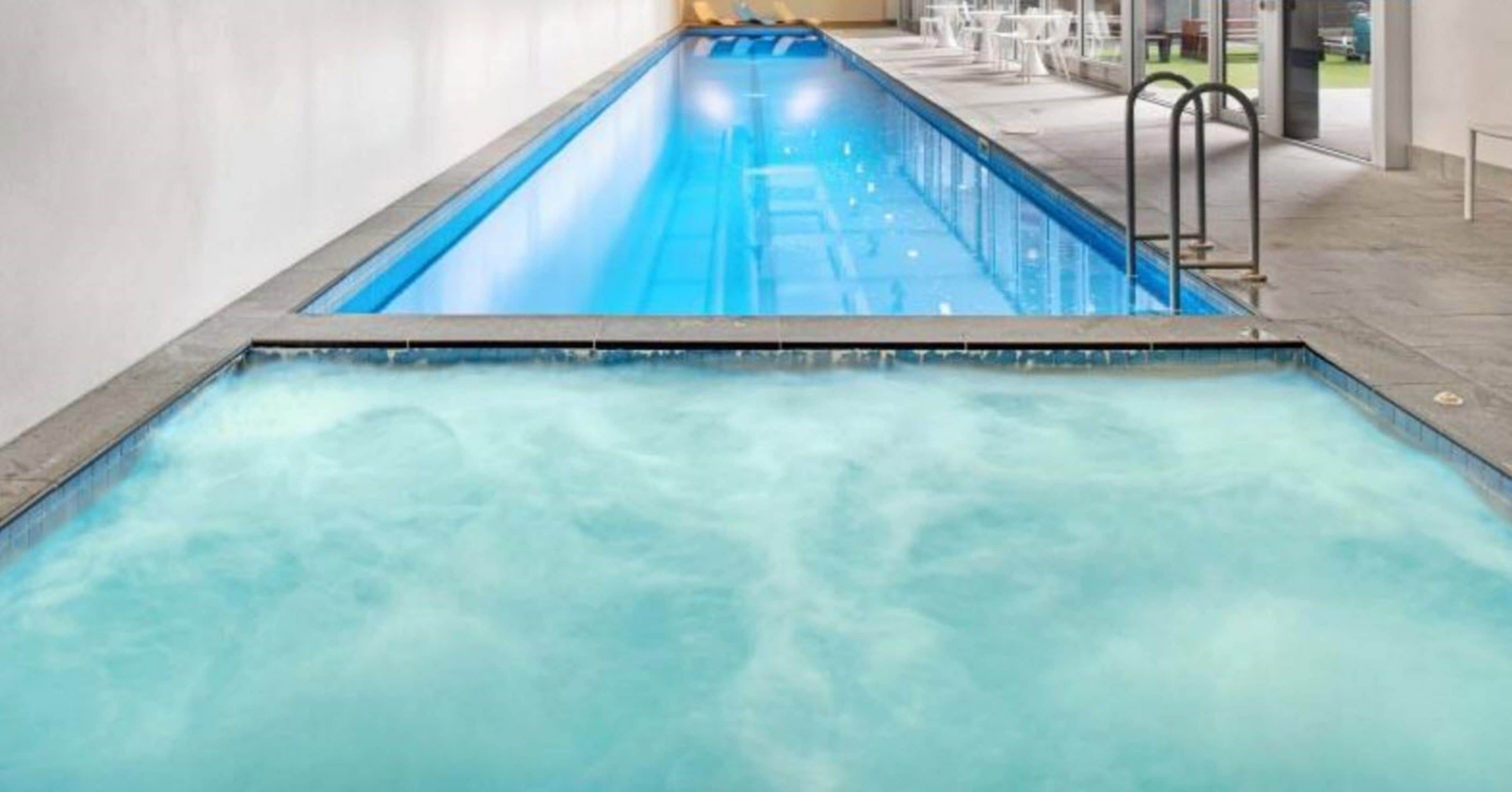 A swimming pool with clear water, a diving board, and a patio area with tables and chairs.