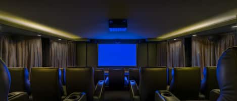 A theater with rows of leather seats, a large screen, and a ceiling projector.